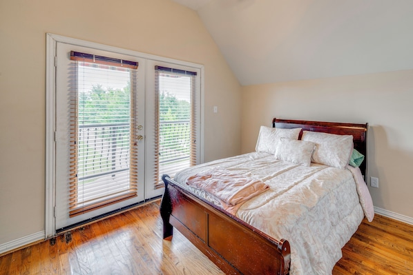 A bedroom with a wooden bed, a sliding glass door, and a sloped ceiling. - Red Oak Group Getaway w/ Yard + Patio (Red Oak)