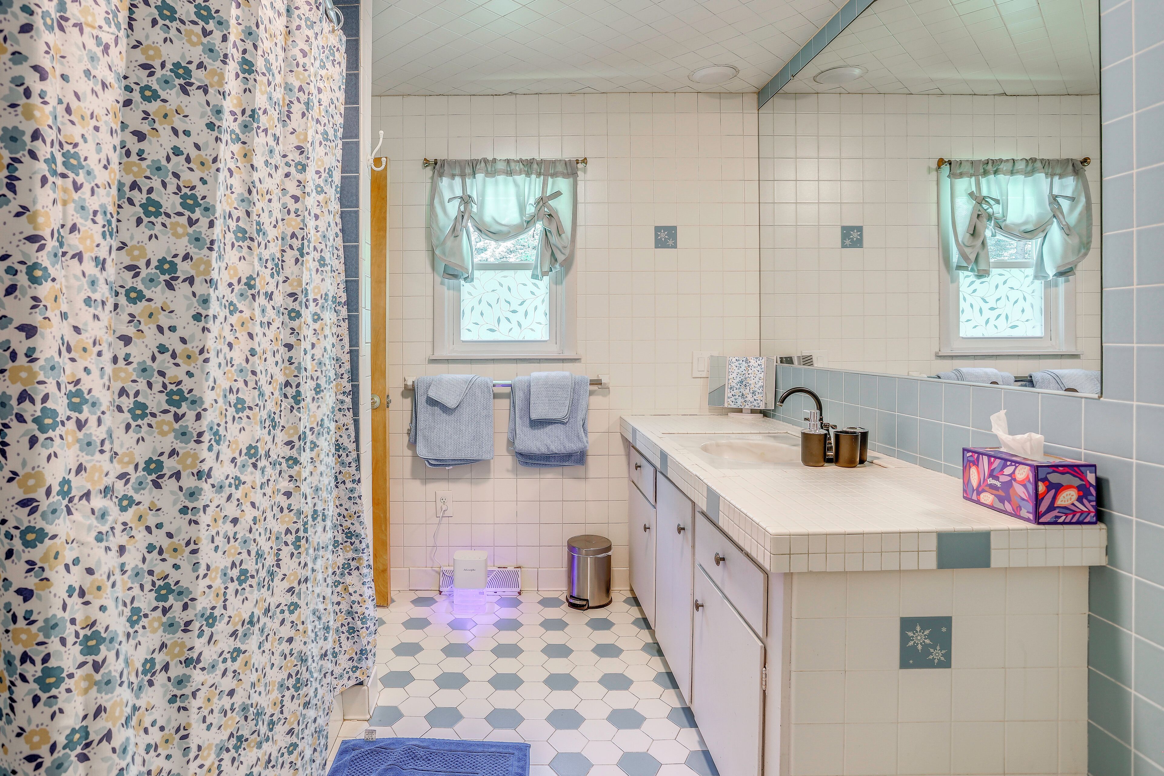 Ein Badezimmer mit gefliestem Boden, einem Waschbecken, einem Spiegel und einer Duschvorhang.