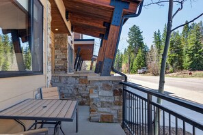 A patio with a table and chairs, stone walls, and a view of a road and trees. - Arrow At Winter Park Unit 256 Downtown mt views, private HT, garage parking (Winter Park)