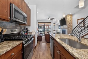Eine Küche mit Granit-Arbeitsplatten, Edelstahlgeräten, Holzschränken und einer Wandverkleidung aus Stein.