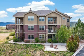 A multi-story residential building with balconies, a patio area with outdoor seating, and a view of the landscape. - Spacious 1 bed, ground floor, private patio (Granby)