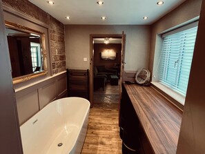 Ein Badezimmer mit Badewanne, Spiegel, Waschtisch aus Holz und einem Fenster mit Jalousien.