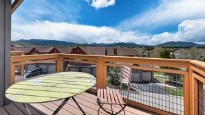 Ein Balkon mit Tisch und Stuhl mit Blick auf eine Wohngegend, mit Häusern und Bergen.