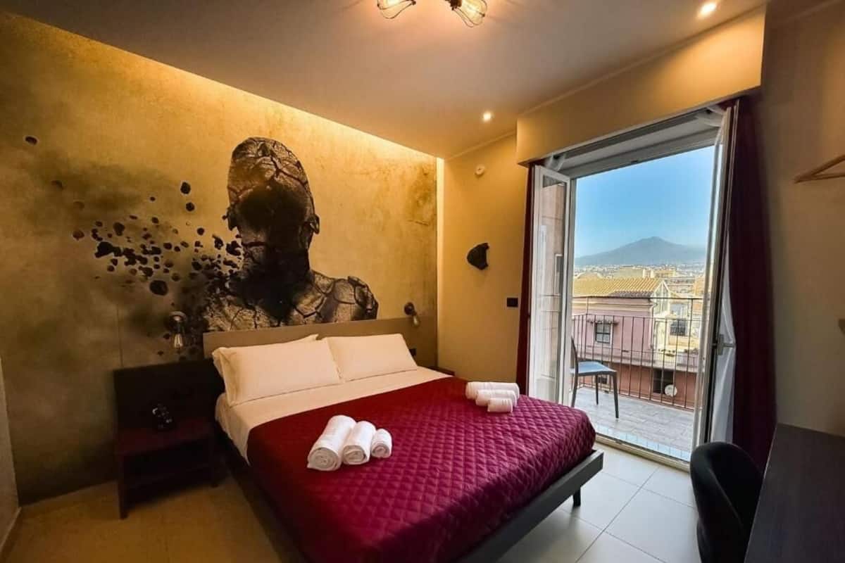 A hotel room with a large bed, a view of the city through a sliding door, and a wall-mounted sculpture.
