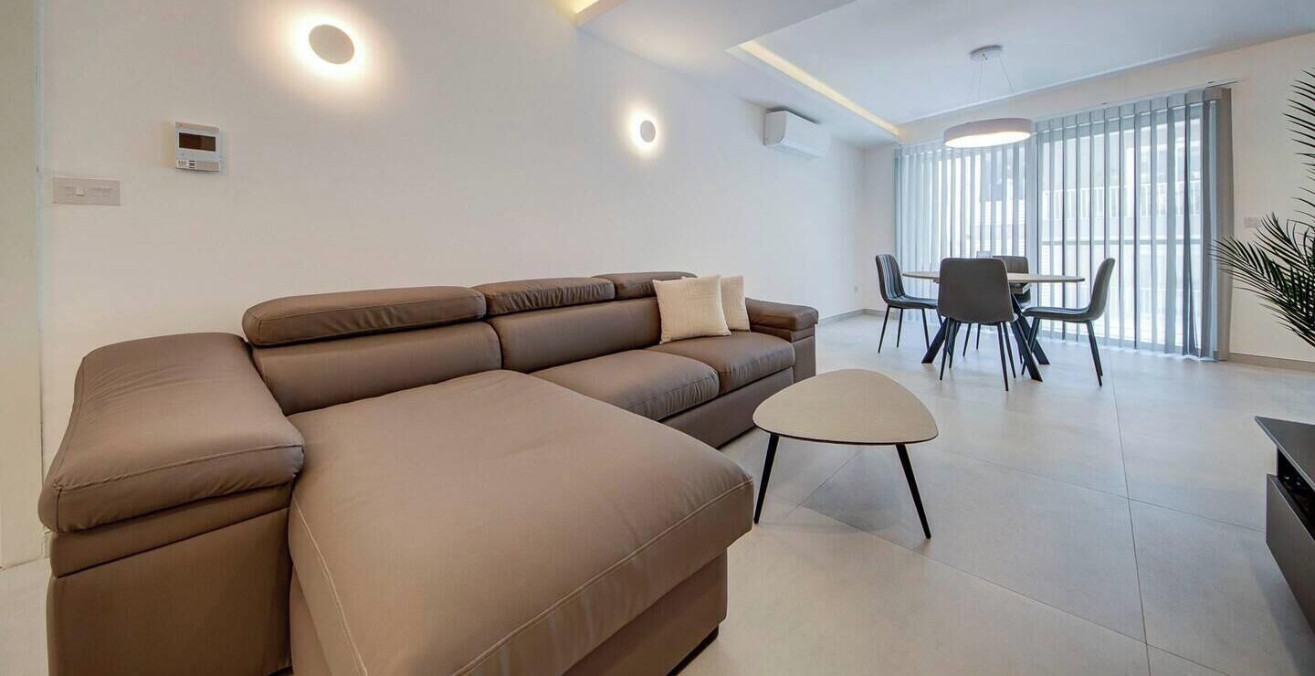 Una sala de estar moderna con un sofá modular, una mesita redonda y un comedor con sillas.