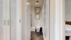 A narrow hallway leading to a bathroom with a toilet, a mirror, and a shower. - Bright Duplex Flat in the Desired Area of Euston (London)