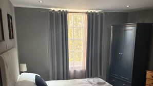 Ein Schlafzimmer mit Bett, Kleiderschrank, Nachttisch und einem Fenster mit Vorhängen.