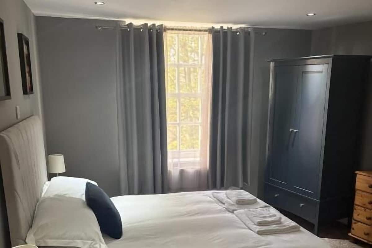 A bedroom with a bed, a wardrobe, a nightstand, and a window with curtains.