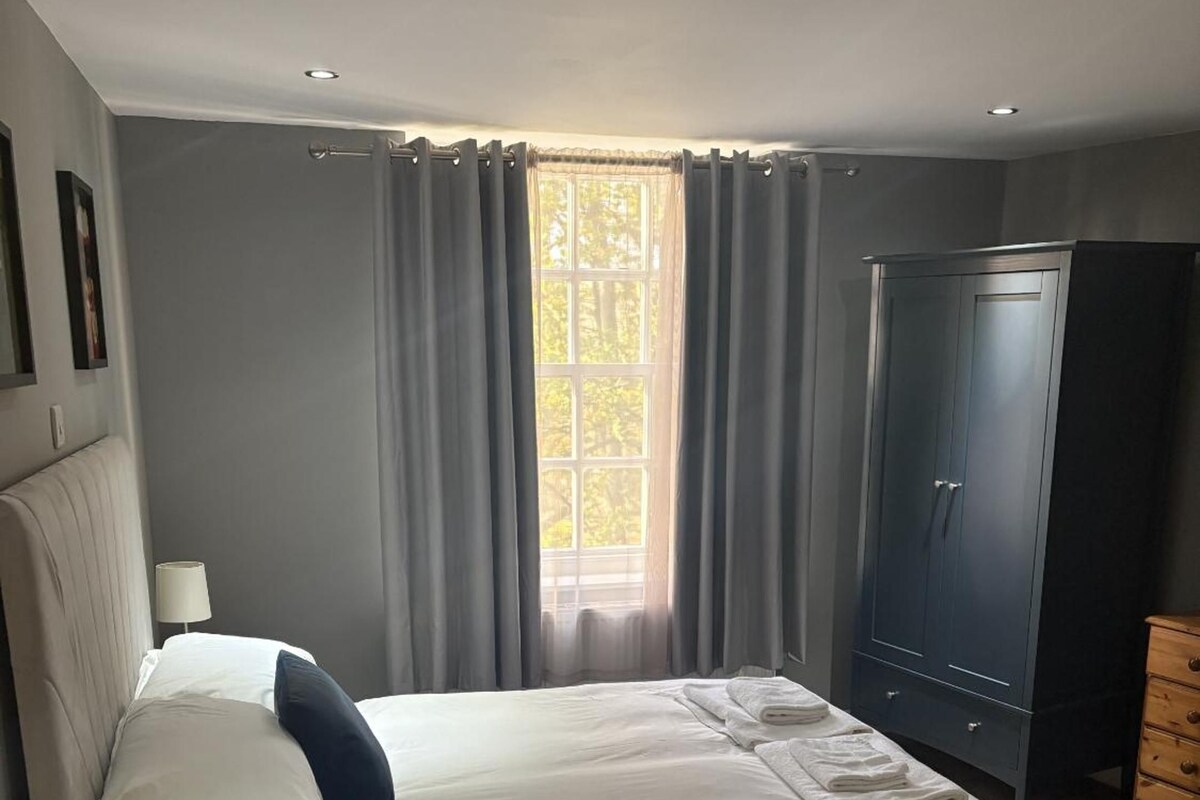 A bedroom with a bed, a wardrobe, a nightstand, and a window with curtains.