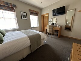 A bedroom with a bed, a desk, a chair, a TV, and a mirror.