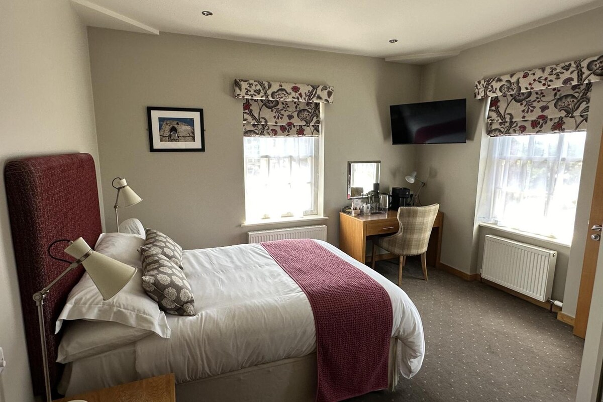 A hotel room with a bed, a desk, a chair, a TV, and a window with curtains.