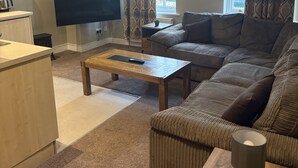 Ein Wohnzimmer mit einer Couch, einem Couchtisch, einem Fernseher, einer Uhr und einem Fenster mit Vorhängen.
