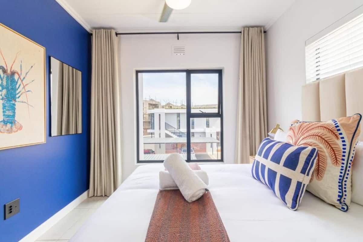 Una habitación de hotel con un ventanal grande, una cama con almohadas, una obra de arte en la pared y un ventilador de techo.