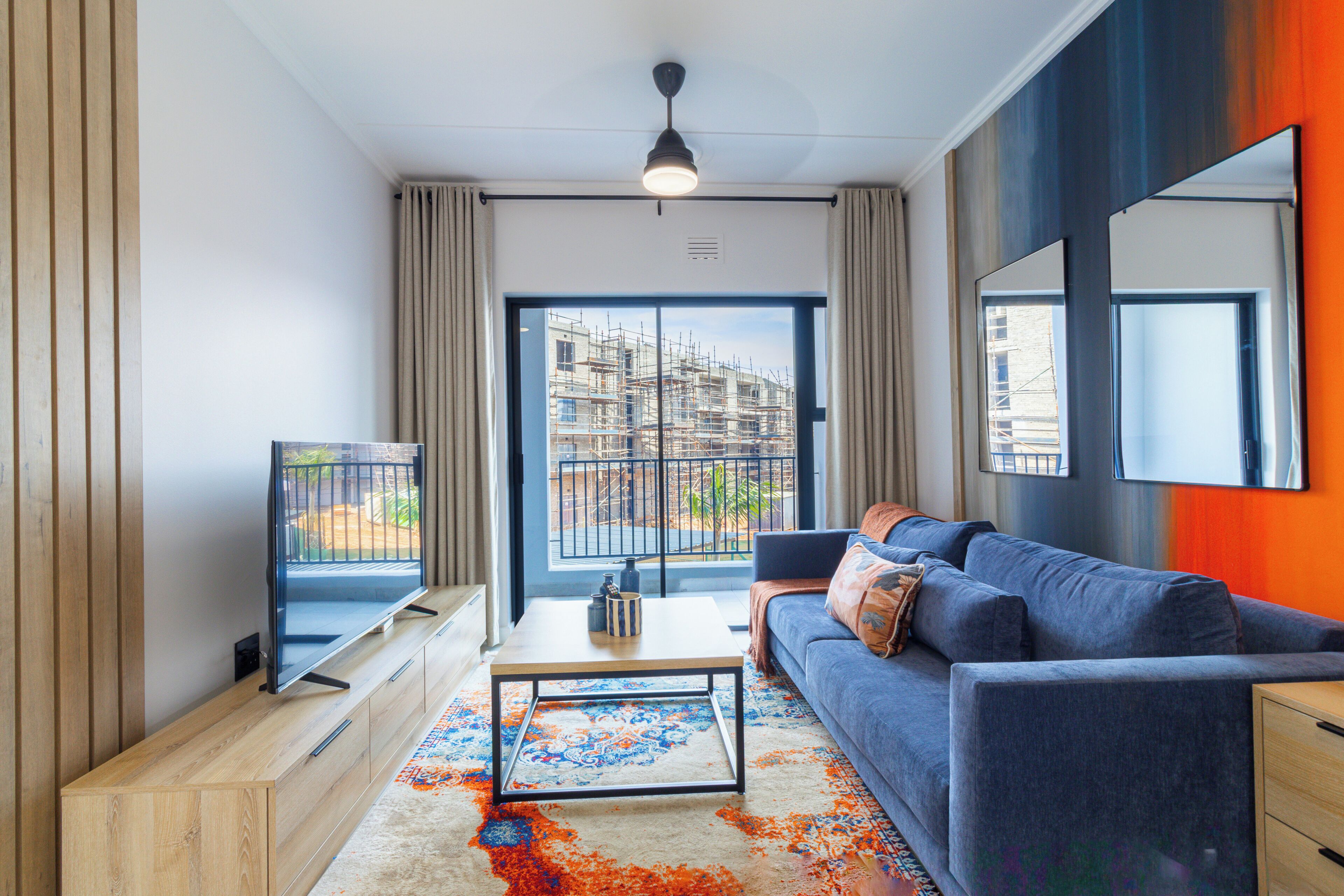 A modern living room with a television, sofa, coffee table, and a view of a building under construction.