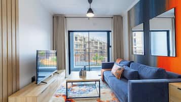 A modern living room with a television, sofa, coffee table, and a view of a building under construction.
