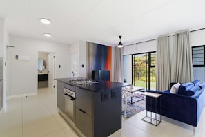 Una cocina moderna con una isla central, un comedor con sofá azul y un amplio ventanal con cortinas.