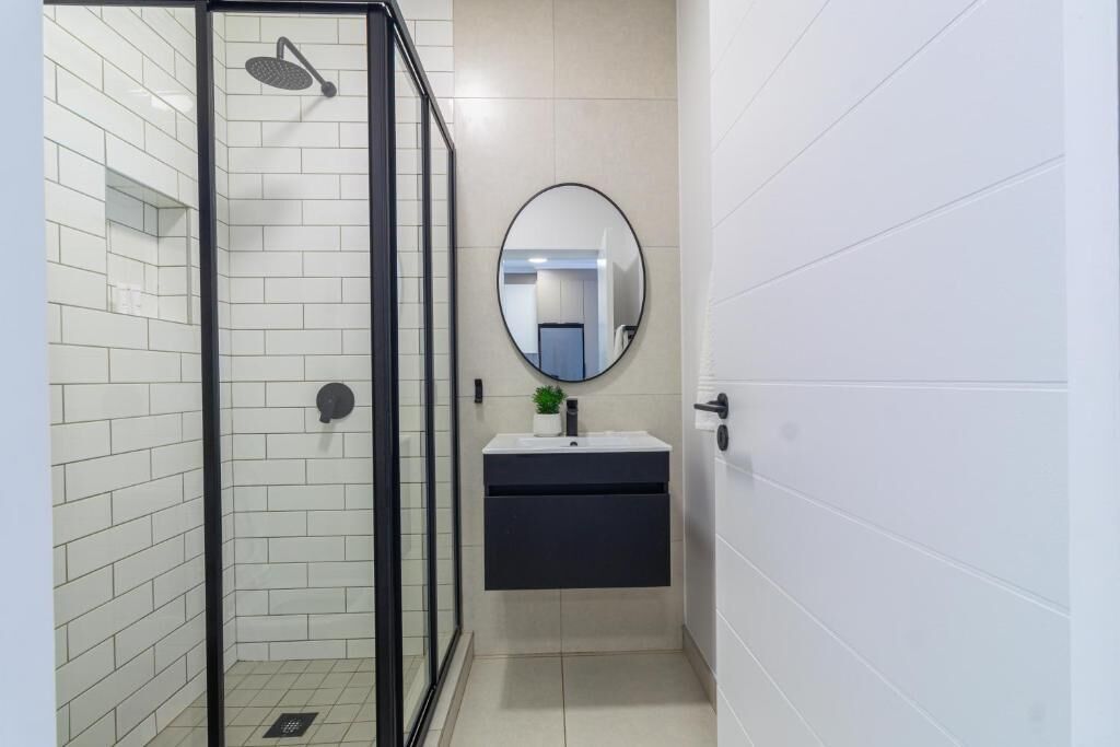 A bathroom with a glass-enclosed shower, a round mirror, and a black vanity.