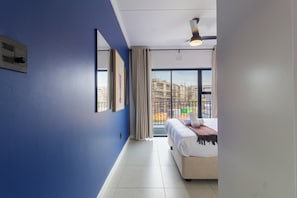 Habitación de hotel con cama, ventana que da a una construcción y ventilador de techo.