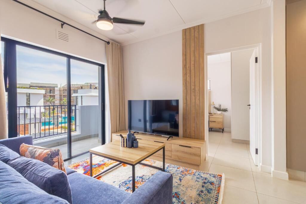 A modern living room with a sofa, coffee table, TV, and a view of a swimming pool.
