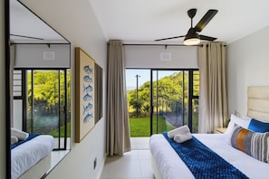 A hotel room with a bed, a ceiling fan, and a large window with a view of greenery. - Ballito Life Estate (Ballito)