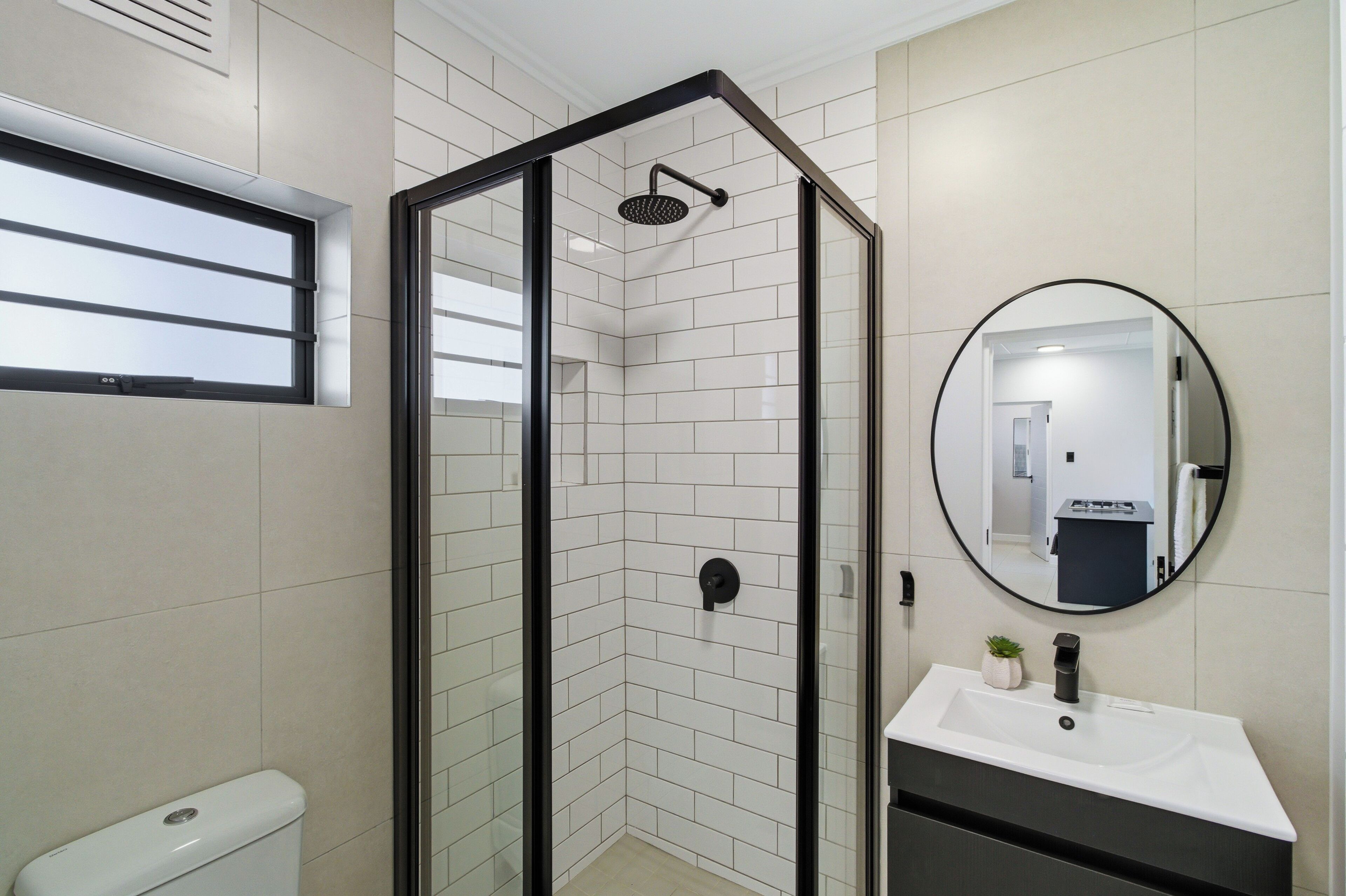 Un baño moderno con cabina de ducha de vidrio, un lavamanos blanco y un espejo redondo.