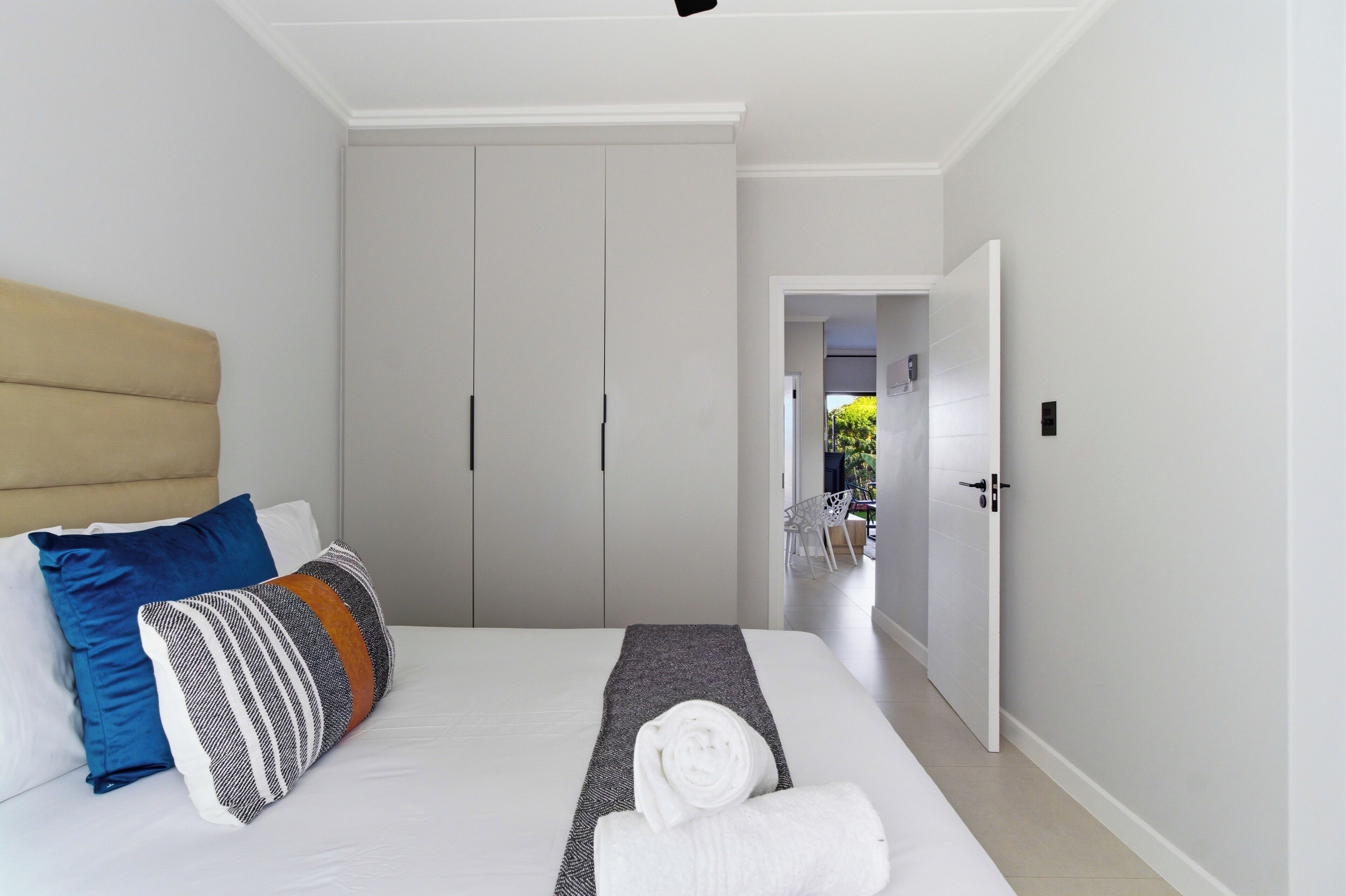 Un dormitorio con cama, almohadas, cabecera, armario y puerta que da a otra habitación.