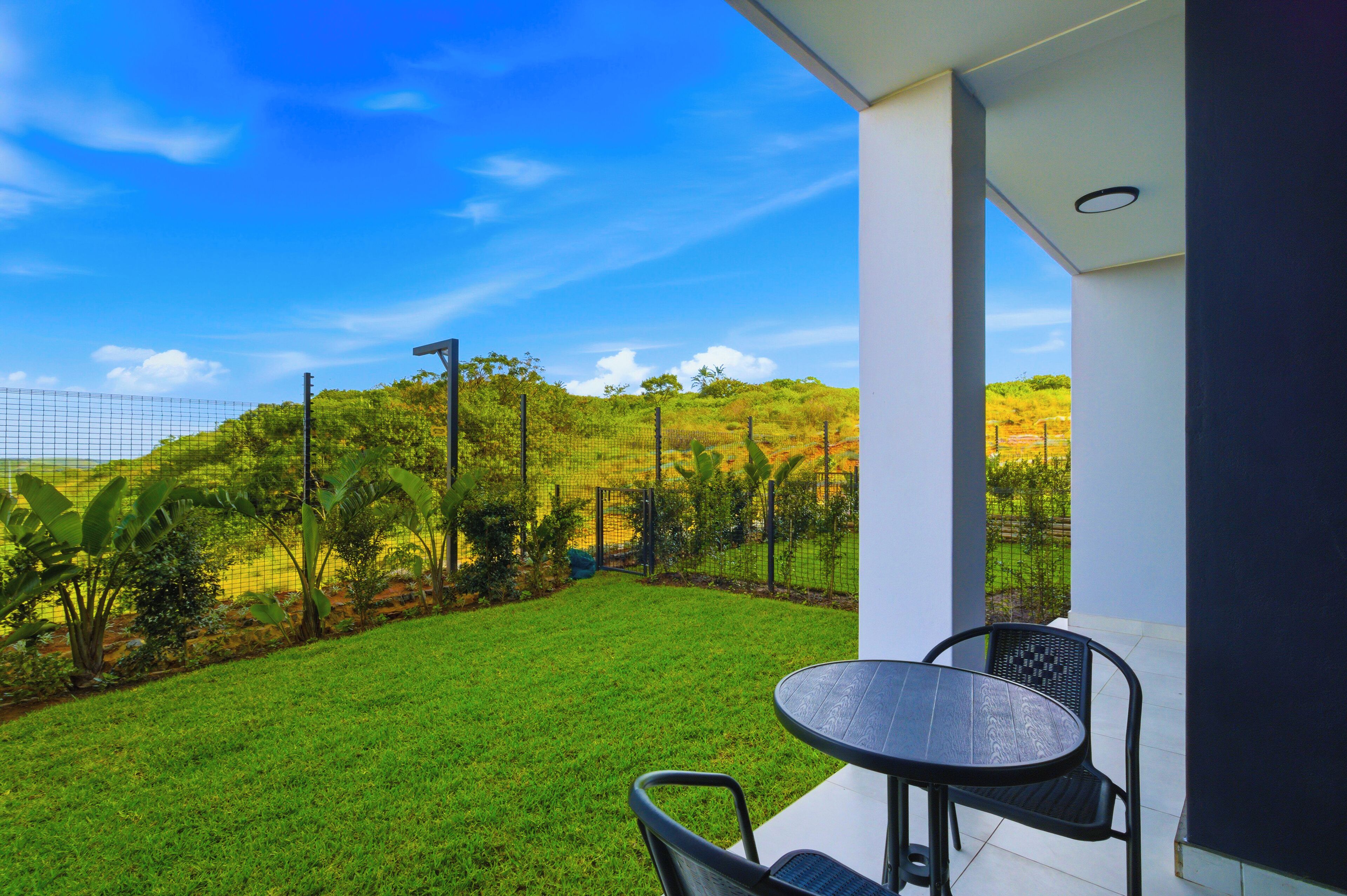 Varanda com mesa e cadeiras, vista para um gramado bem cuidado e paisagem montanhosa.