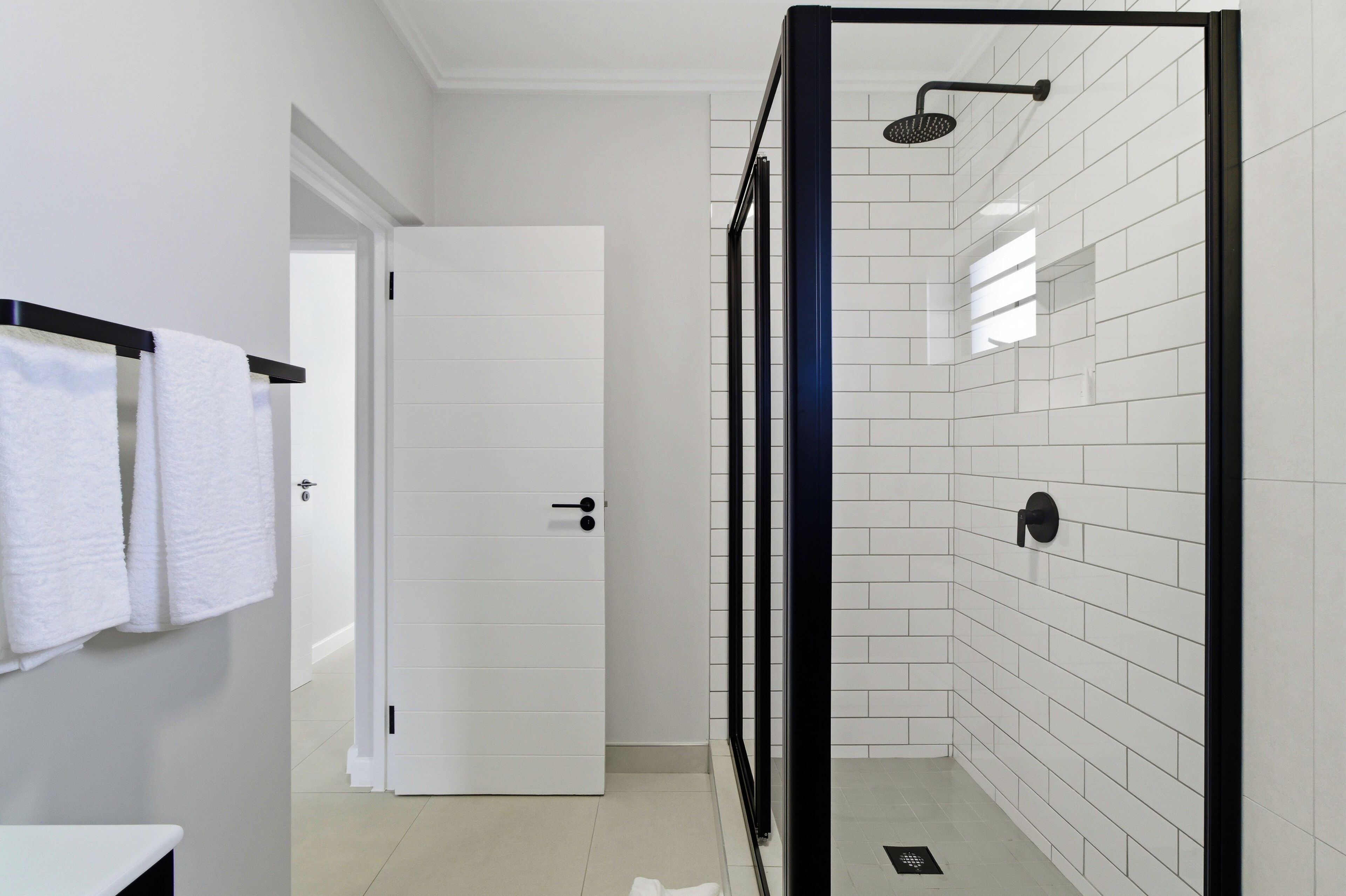 Uma casa de banho moderna com paredes revestidas a azulejos brancos, um chuveiro com cabine de vidro e uma porta branca.