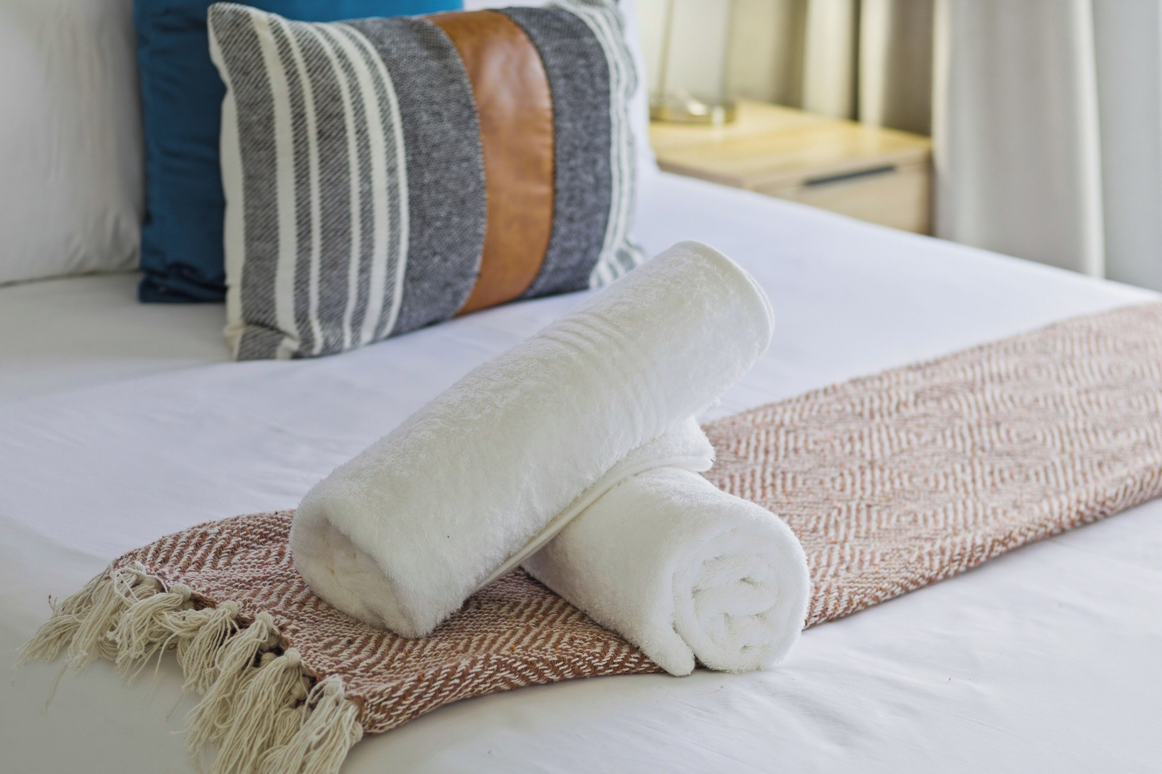 A neatly made bed with a rolled white towel, a striped pillow, and a brown woven throw.