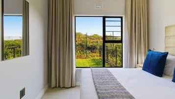 A hotel room with a large bed, a view of greenery through a sliding door, and a ceiling fan.