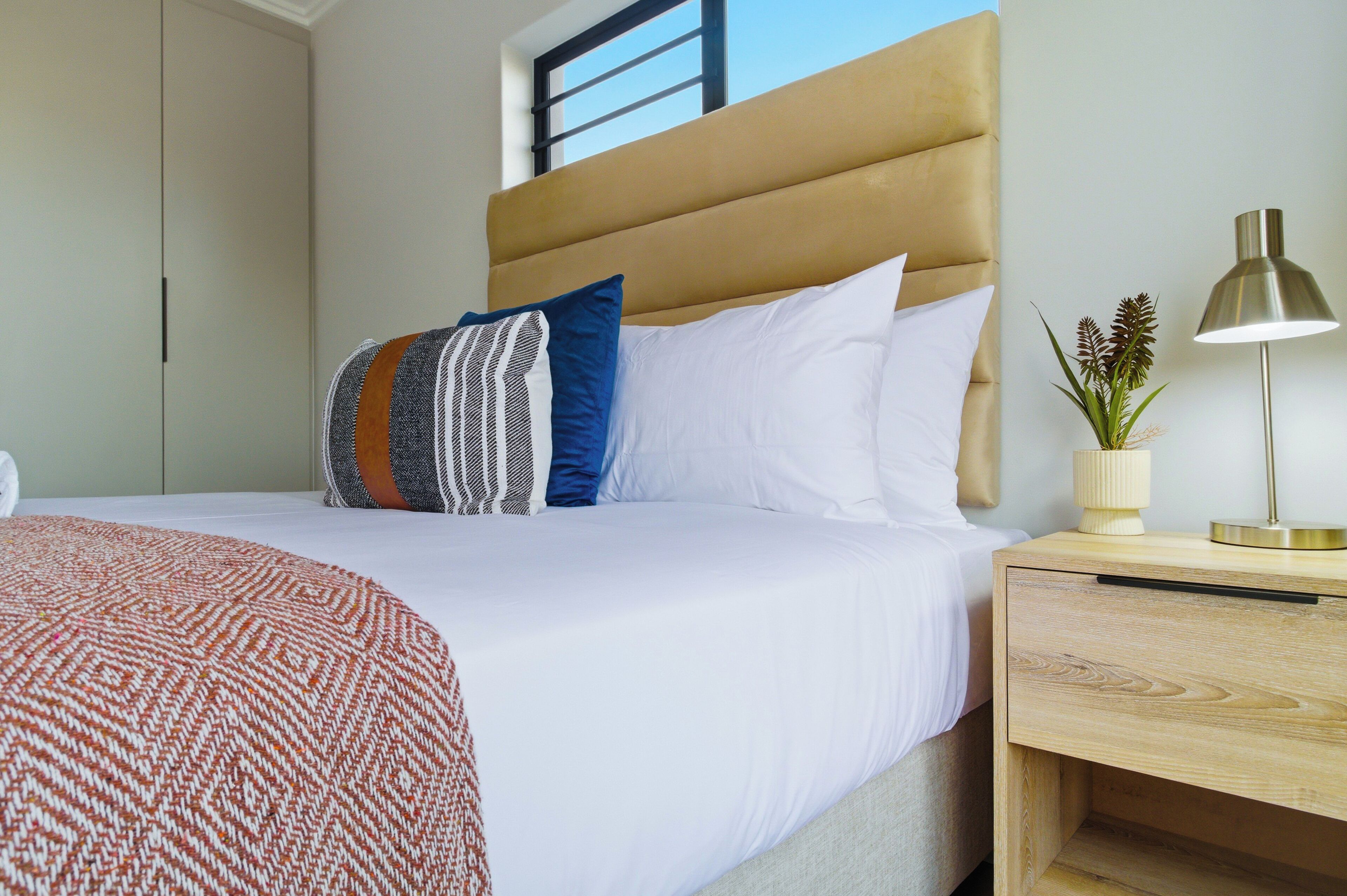 A hotel room with a bed, a nightstand with a lamp, a window, and a wardrobe.