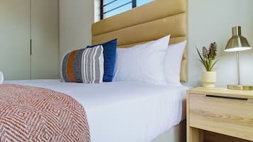 Een hotelkamer met een bed, een nachtkastje met lamp, een raam en een kast.