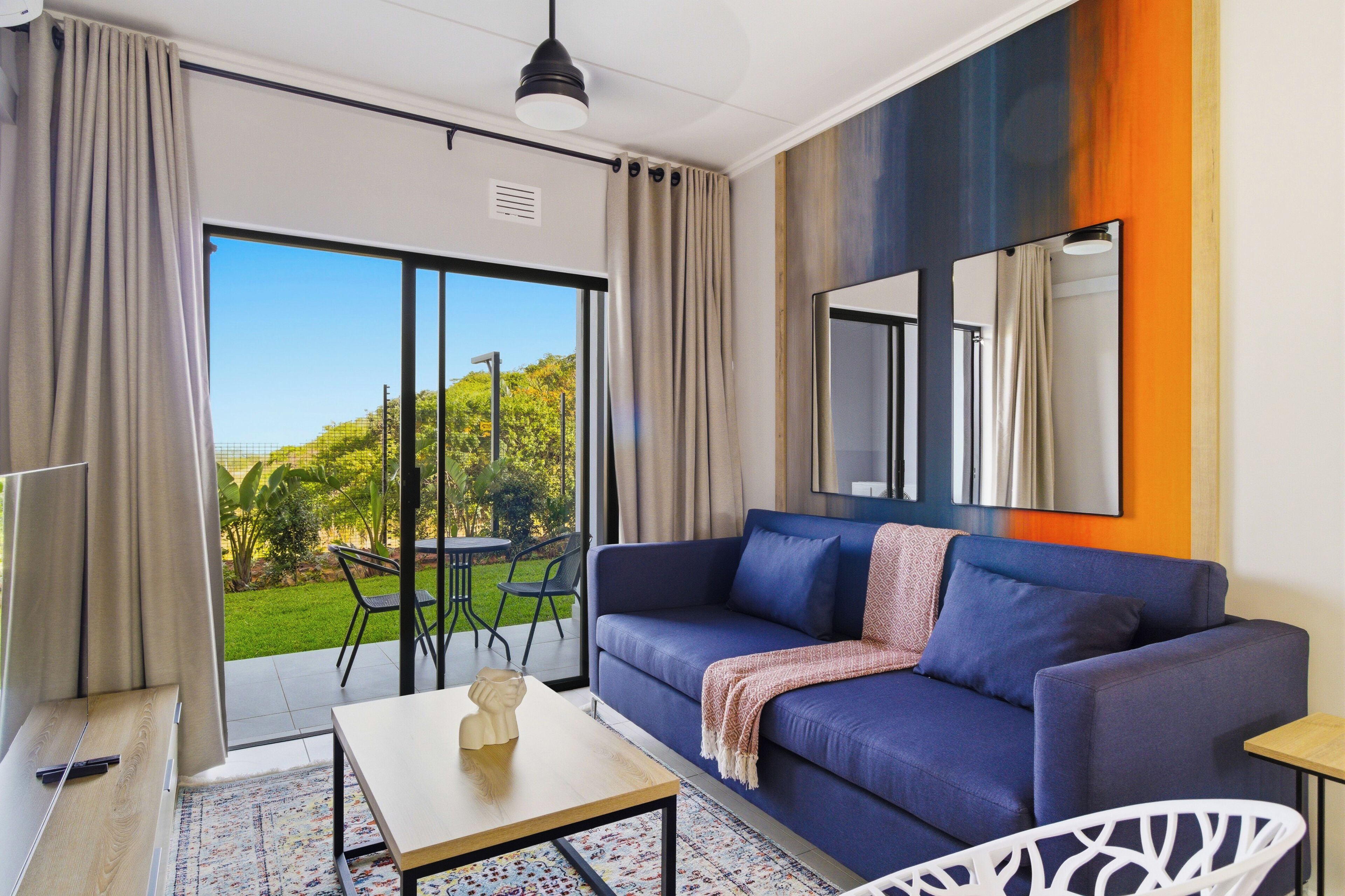 A modern living room with a blue sofa, a coffee table, and a view of a garden through a sliding glass door.