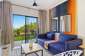 Una sala de estar moderna con un sofá azul, una mesa de centro y vistas a un jardín a través de un ventanal corredero.