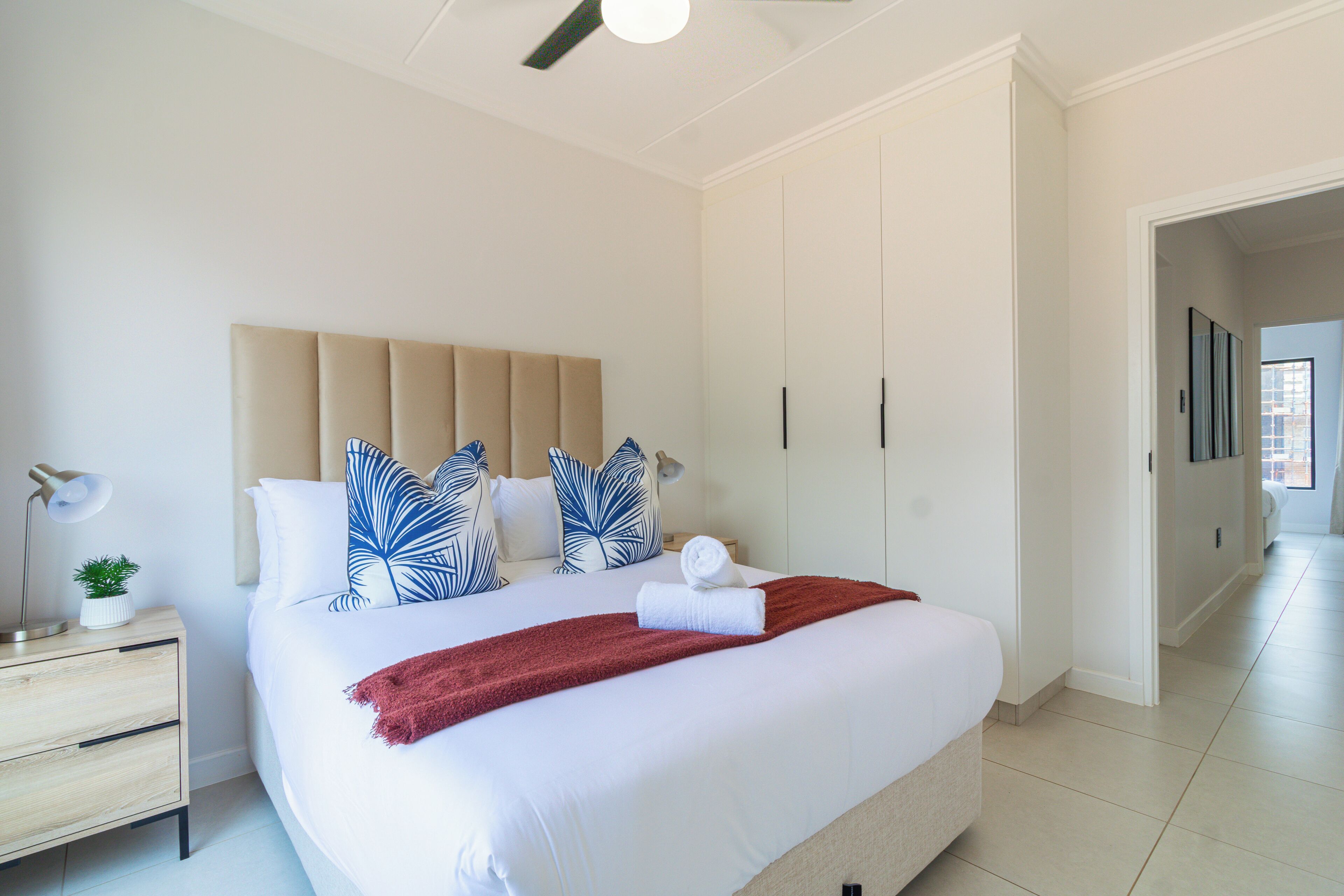 A hotel room with a bed, a nightstand, a lamp, and a view of the hallway.