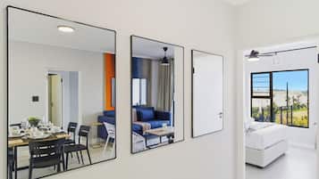 A modern hotel room with a dining area, a living space with a sofa and a coffee table, and a large window offering a view.