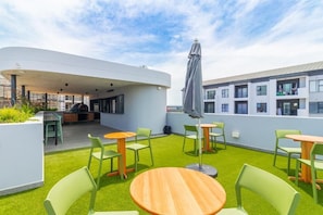 A rooftop terrace with green chairs, wooden tables, and a barbecue area. - Ballito Life Estate (Ballito)
