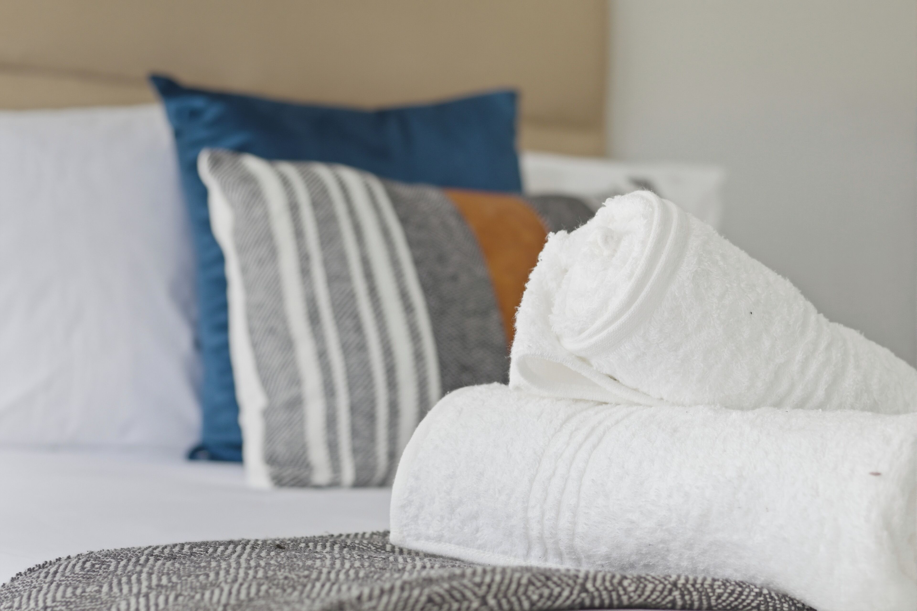 A neatly made bed with a white towel rolled up, a striped pillow, and a blue pillow.