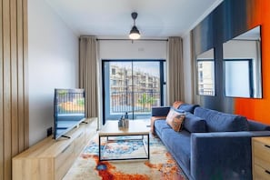 A modern living room with a sofa, coffee table, TV, and a view of a building under construction. - Ballito Life Estate (Ballito)