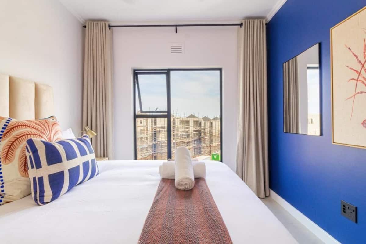 Habitación de hotel con una cama grande, vistas de edificios a través de la ventana y una pared azul.