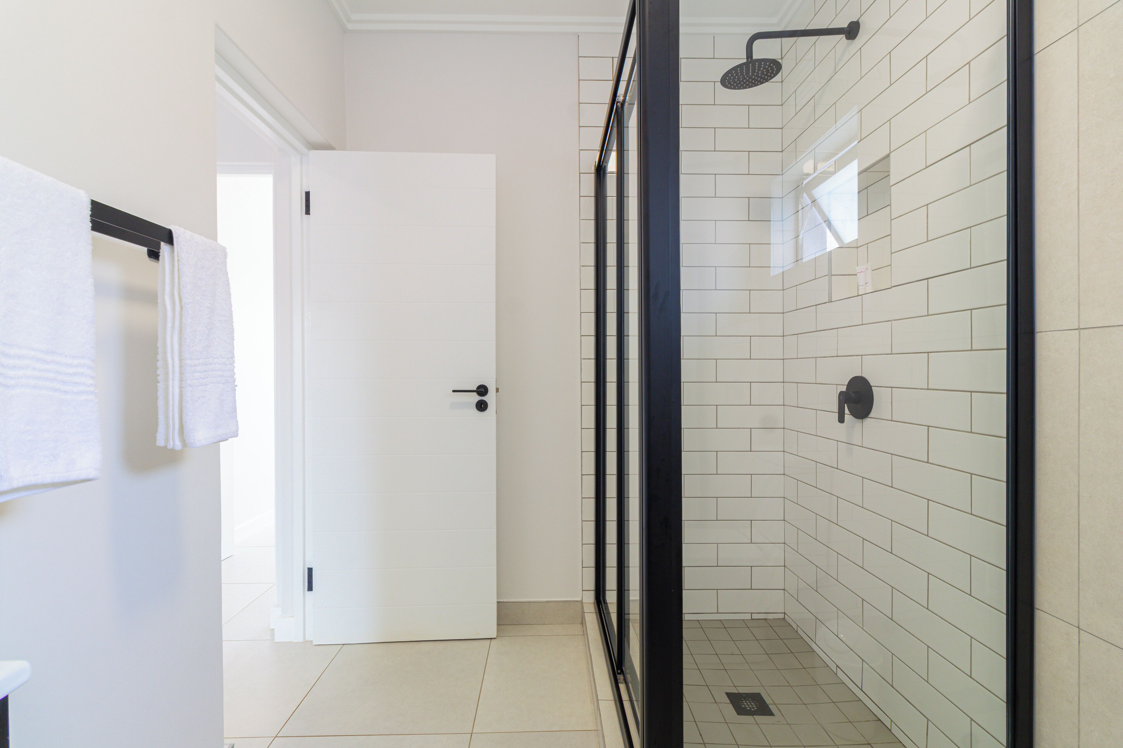A bathroom with white tiled walls, a glass shower enclosure, and a white door.