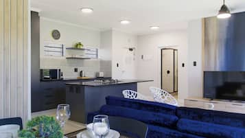 A modern kitchen with a central island, a dining area with a blue sofa, and a TV in the living room.