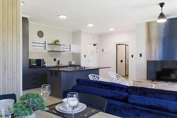 A modern kitchen with a central island, a dining area with a blue sofa, and a TV in the living room. - Ballito Life Estate (Ballito)