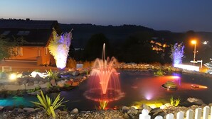 A nighttime outdoor area with a pond, illuminated plants, and a small island with a boat. - Studio with Volcano View at Maarberg Resort in Schalkenmehren by the Lake (Schalkenmehren)