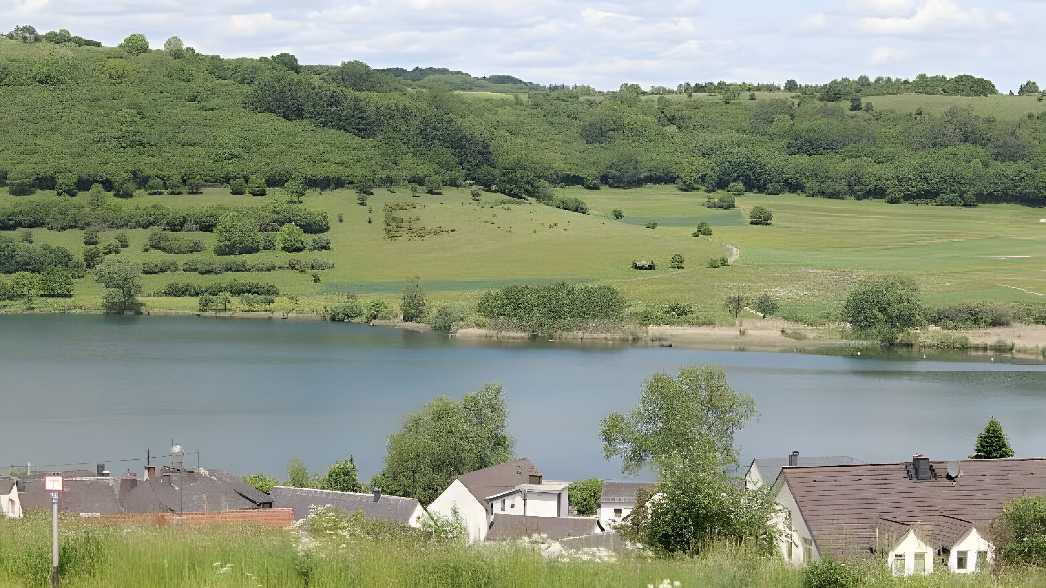 En sø omgivet af grøn vegetation og enkelte huse i forgrunden.