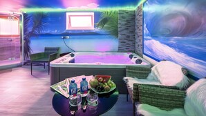 A room with a hot tub, a table with drinks and fruit, and a beach mural. - Studio with Volcano View at Maarberg Resort in Schalkenmehren by the Lake (Schalkenmehren)
