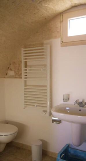 Un baño con inodoro, lavamanos, ventana y un perchero para toallas.