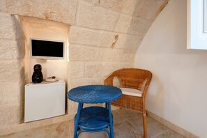 A room with a stone wall, a white appliance, a blue wicker chair, and a television mounted on the wall. - Alloro Double Room in Elegant Villa near Beaches and Countryside (Macchia al Monte)