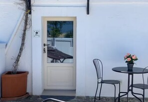 En hvid dør med et glasfelt, en potteplante og et bord med stole foran en bygning.