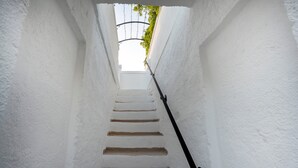Eine schmale, weiße Treppe mit schwarzer Handläufung führt zu einem überdachten Bereich mit Grünpflanzen darüber.